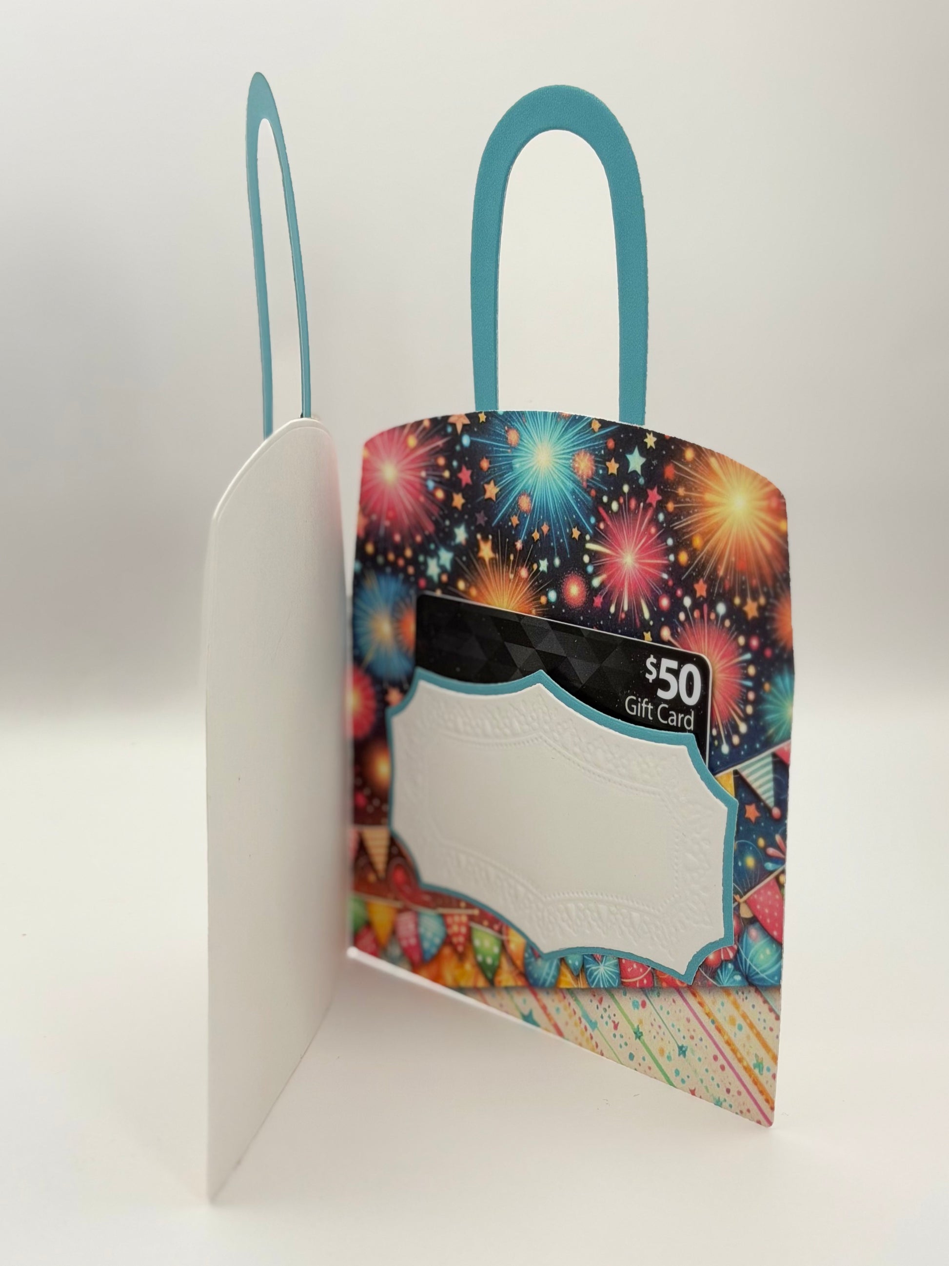 A novelty gift card holder shaped like a shopping bag, featuring a colorful fireworks pattern on one side, a white embossed center panel, and a black Gift Card placeholder window, with teal handles on a white background.
