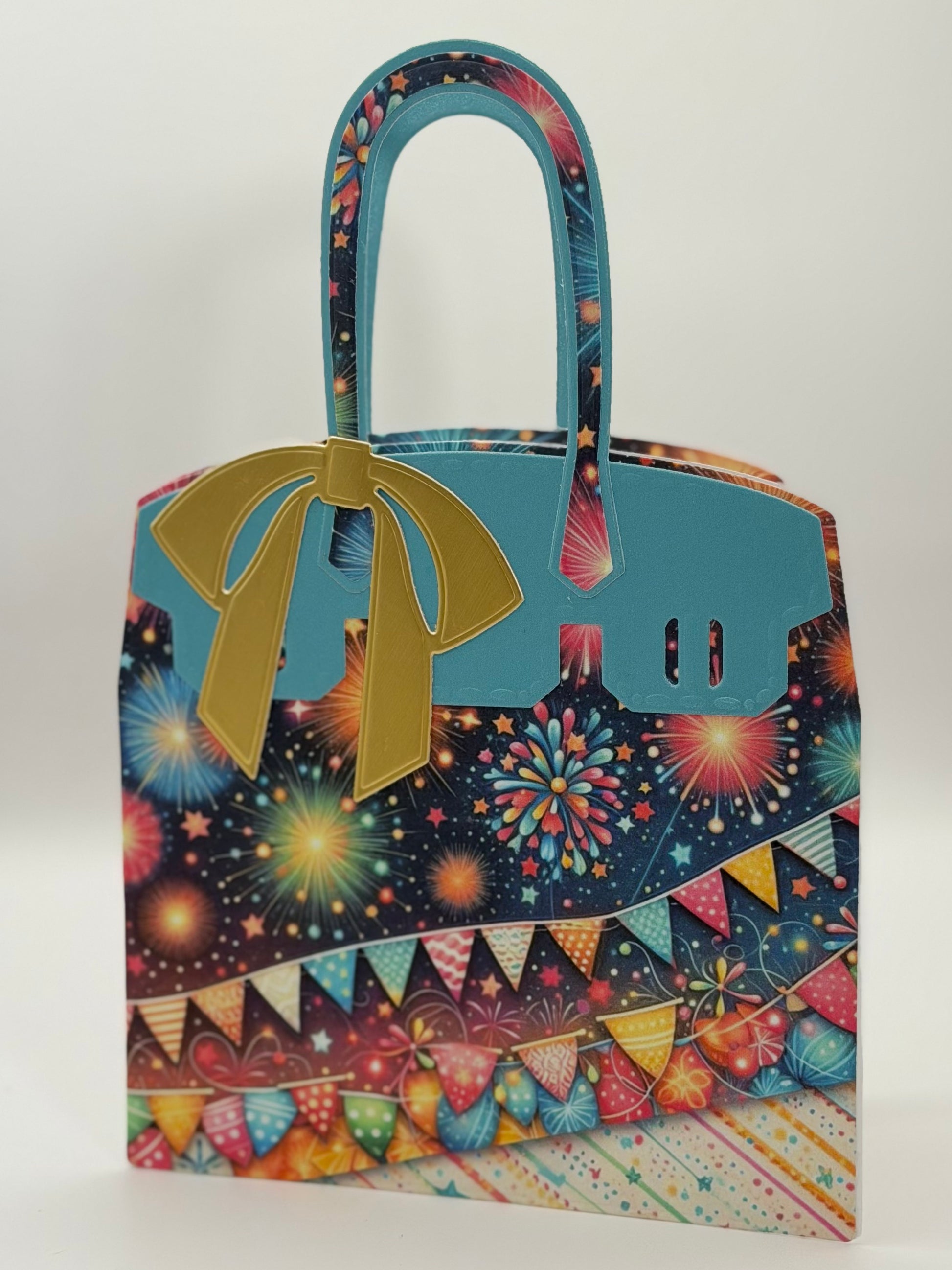A novelty tote bag designed to look like a luxury handbag, featuring a light blue faux leather front and handle, a gold bow, and a busy multicolor fireworks and bunting pattern on a dark navy background.
