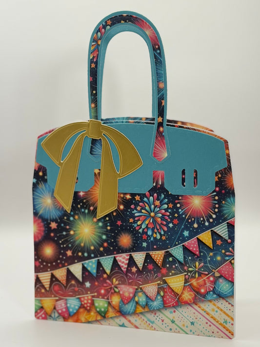 A novelty tote bag designed to look like a luxury handbag, featuring a light blue faux leather front and handle, a gold bow, and a busy multicolor fireworks and bunting pattern on a dark navy background.