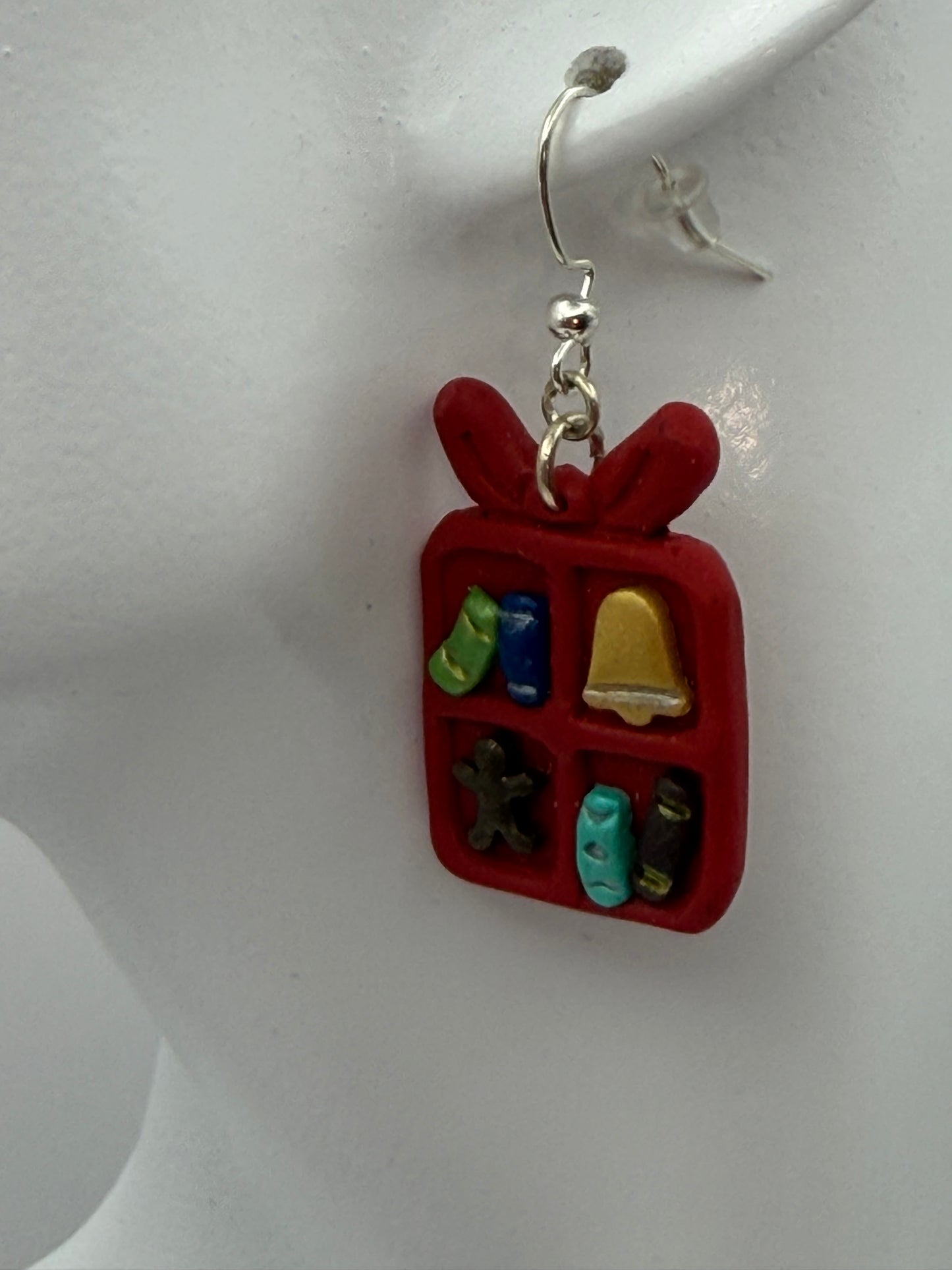 A pair of red gift box dangle earrings with small holiday-themed charms inside, hanging from silver hooks on a white display card that reads 'Charmed and Crowned'.